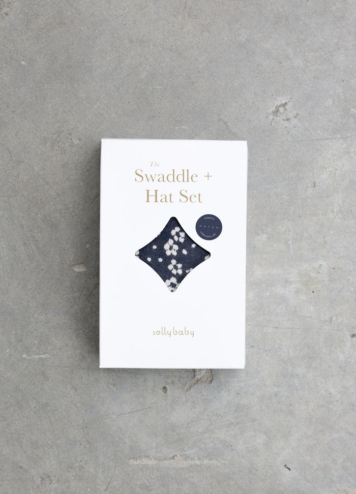 White packaging box featuring a navy blue floral baby swaddle and matching hat set illustration.