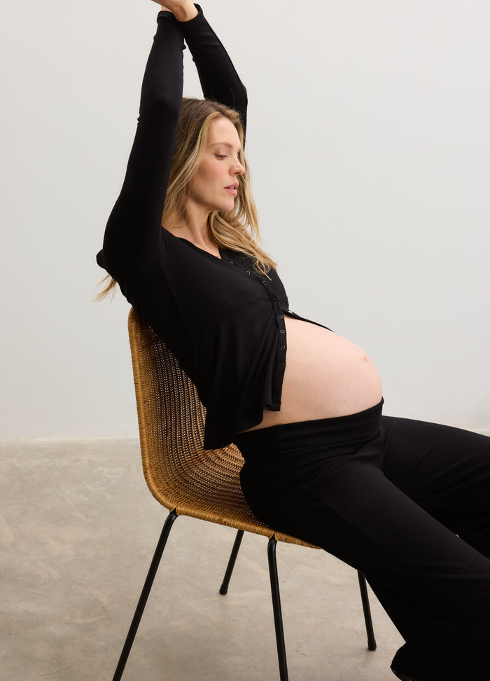 Black soft ribbed maternity top with long sleeves paired with matching ribbed maternity leggings on pregnant model sitting.