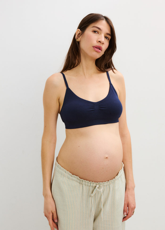 Navy blue maternity bra with thin adjustable straps on pregnant woman with loose beige pants.