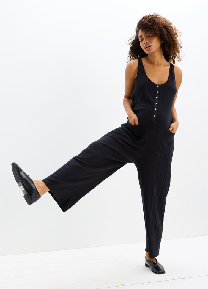 Black sleeveless maternity jumpsuit with buttons down front and wide legs, worn with black flats.