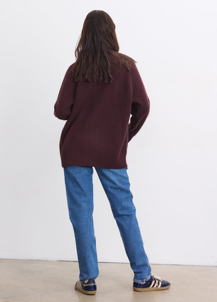 Long burgundy cashmere cardigan with a relaxed fit, worn over casual blue jeans and sneakers.