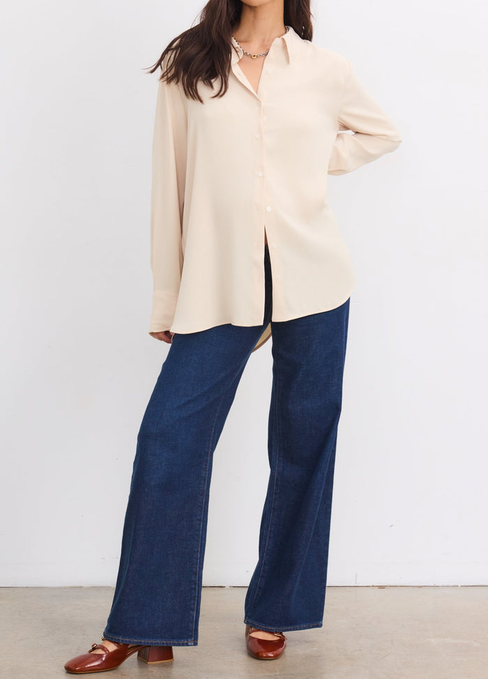 Sandshell maternity buttondown shirt with drapey fit worn by pregnant model with blue wide-leg jeans.