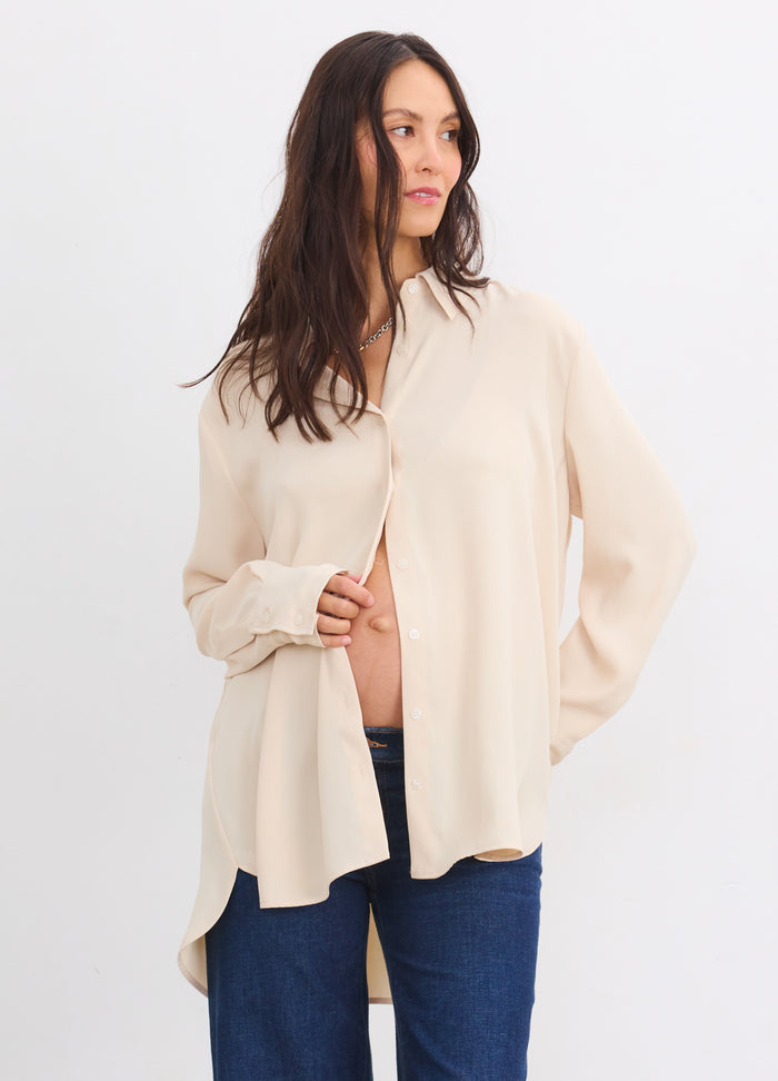 Sandshell maternity buttondown shirt with drapey fit worn open over pregnant belly, paired with blue jeans.