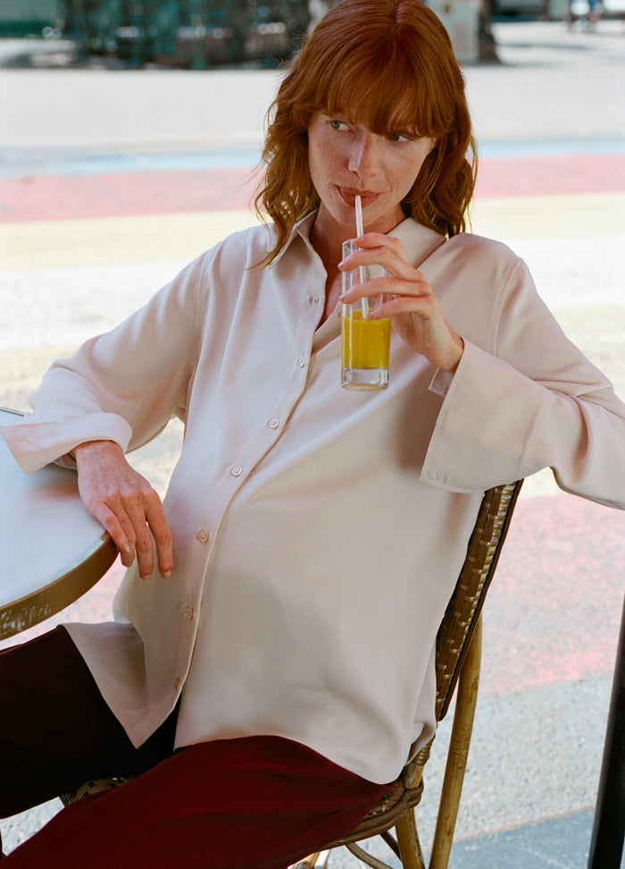 Light pink drapey maternity buttondown shirt with long sleeves and a collar, worn over black pants.