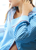 Light blue cotton maternity pajama top with dark thin vertical stripes and red piping on collar and cuffs.