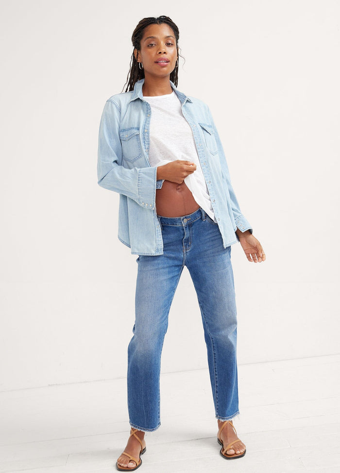 The Denim Maternity Shirt - Light wash denim maternity shirt with rolled sleeves, worn open over a white tank top during pregnancy.