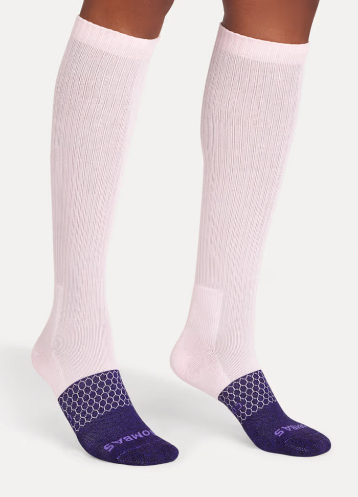 Pair of knee-high maternity compression socks in soft pink with dark purple textured foot soles.