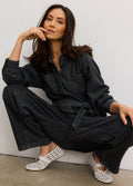 Pregnant woman wearing washed black drapey denim maternity jumpsuit with button-up front and belted waist.