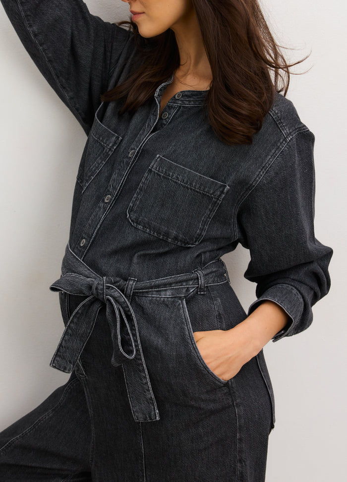Dark gray denim maternity jumpsuit with front buttons, chest pocket, and waist tie belt.