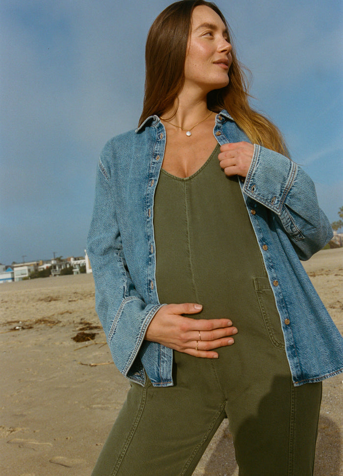 Olive green maternity jumpsuit with V-neck and adjustable straps, paired with loose light blue denim jacket.