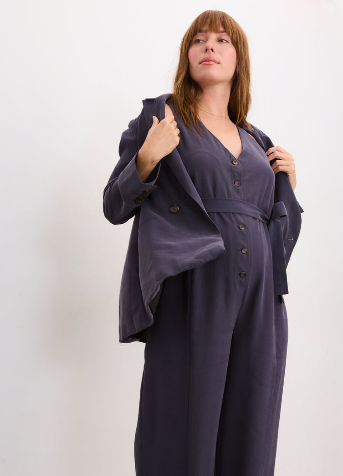 Slate blue maternity jumpsuit with button front and loose long sleeves on a pregnant model.
