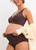 Pregnant woman wearing Demi Fleur Bordeaux maternity high tuck brief and matching bra with cream cardigan draped over arm.