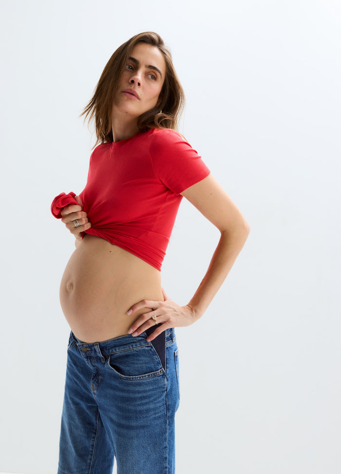 Red short-sleeve ribbed maternity tee paired with blue jeans, highlighting a pregnant belly.
