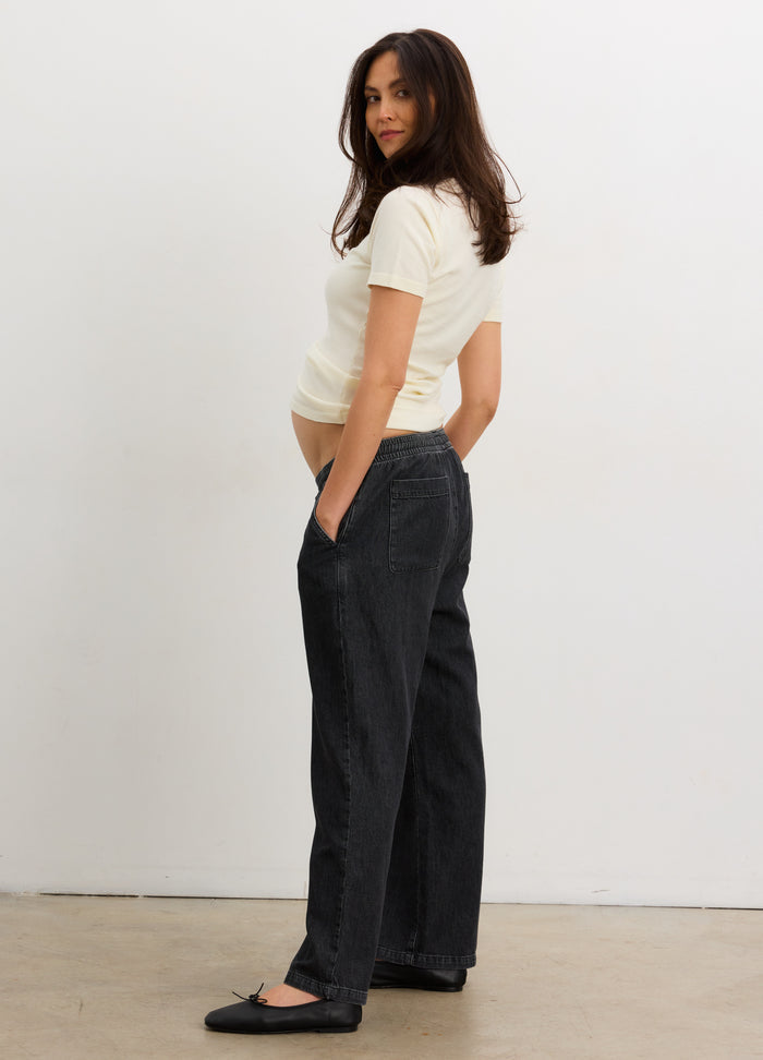 Cream short-sleeve knit maternity tee with subtle ribbed texture, paired with loose black pants.