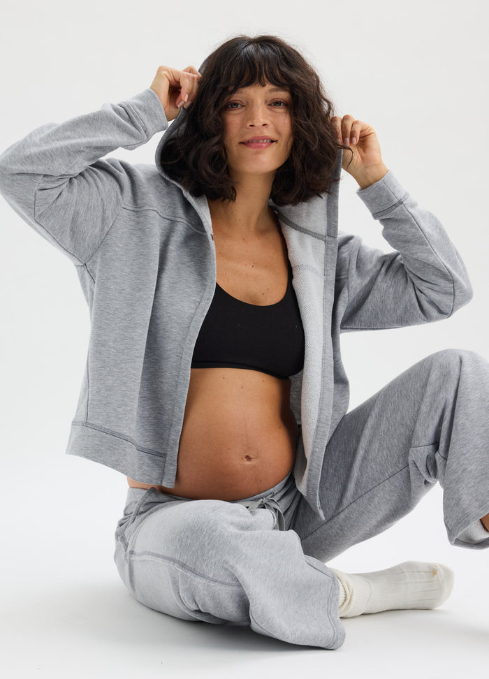 Light grey maternity joggers with matching zip-up hoodie worn over black sports bra on pregnant model.